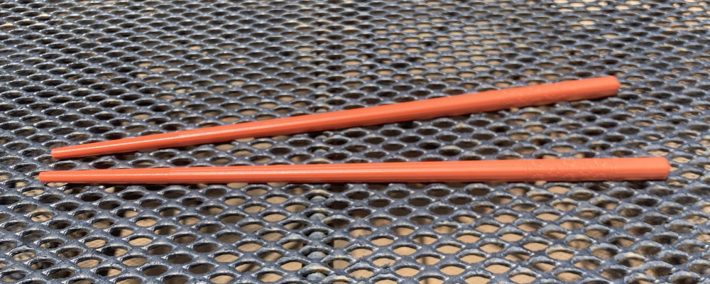 A bright orange set of chopsticks, resting on a table outdoors.