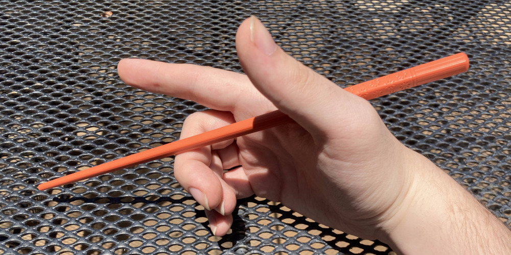 The first stick, resting on my middle finger and placed between my thumb and index finger. My hand is still in the same position.